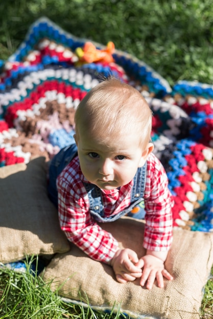 Porträt eines Jungen, der auf einer Decke auf einem frischen Gras in einem Stadtpark im Sommer sitzt