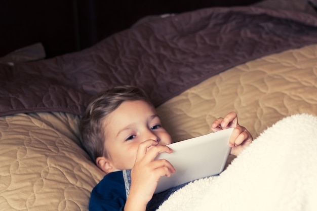 Porträt eines Jungen, der ein digitales Tablet benutzt, während er zu Hause im Bett liegt