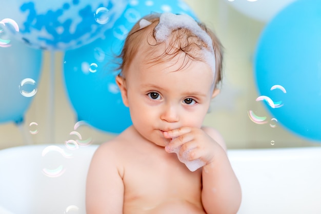 Porträt eines Jungen, der in einem Bad mit Luftballons und Seifenblasen badet, glückliche Kindheit, Kindergeburtstag