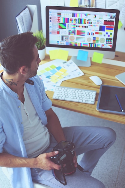 Foto porträt eines jungen designers, der im grafikstudio vor laptop und computer sitzt, während er online arbeitet