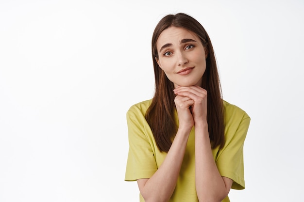 Porträt eines jungen dummen Mädchens, das ein entzückendes Gesicht macht, sich auf die Hände stützt und um etw bittet, bettelt, über schöne Dinge nachdenkt und auf Weiß steht. Platz kopieren