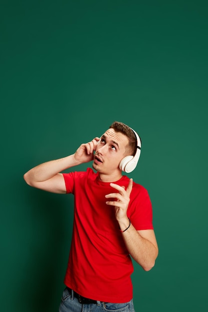 Porträt eines jungen emotionalen Mannes in lässiger Kleidung, der in Kopfhörern posiert, die über grünem Hintergrund isoliert sind Konzept von Emotionen und Musik