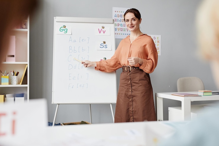 Foto porträt eines jungen englischlehrers, der auf whiteboard mit englischem alphabet zeigt, während er im klassenzimmer steht