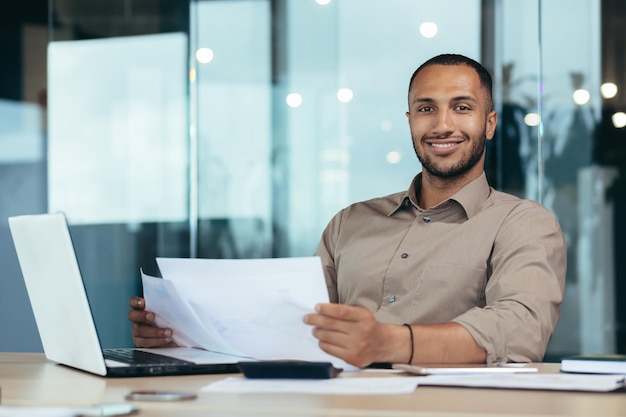 Porträt eines jungen erfolgreichen hispanischen Geschäftsmannes im Büro, der lächelt und in die Kamera schaut