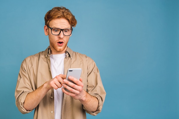 Porträt eines jungen erstaunten, schockierten Mannes beim zufälligen Tippen von SMS. Telefon verwenden.