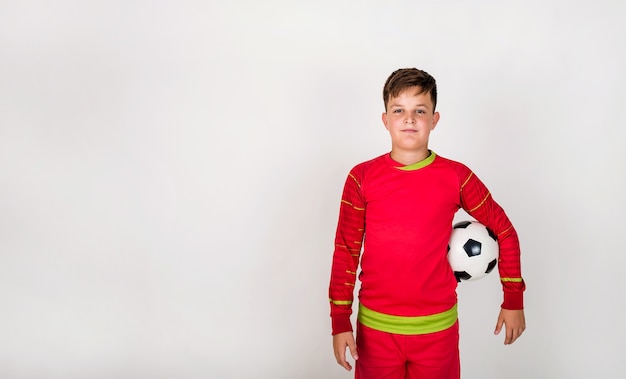 Porträt eines jungen Fußballspielers in roter Uniform, der mit einem Fußball auf weißem Hintergrund mit Platz für Text steht