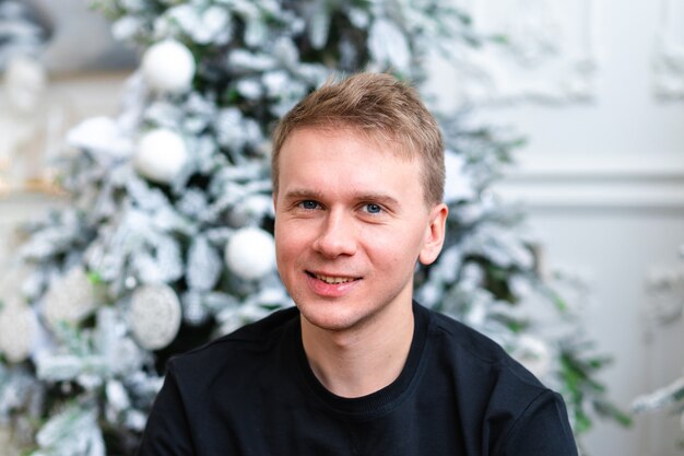 Porträt eines jungen glücklichen blonden Mannes, der über Weihnachtsbaum aufwirft