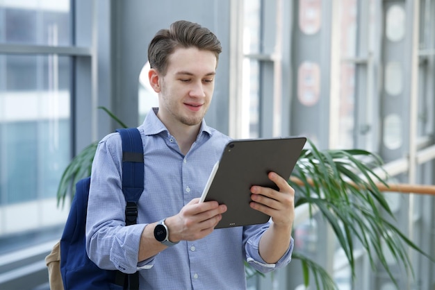 Porträt eines jungen, glücklichen Mannes, gutaussehender Kerl, Universitäts- oder College-Student, schaut auf den Bildschirm von