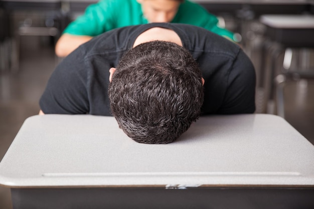 Porträt eines jungen Gymnasiasten gelangweilt und frustriert mit dem Kopf auf seinem Schreibtisch