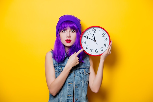 Porträt eines jungen Hipster-Mädchens mit lila Haaren mit großer Uhr auf gelbem Hintergrund