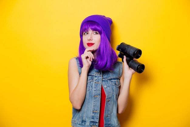 Porträt eines jungen Hipster-Mädchens mit lila Haaren und Fernglas auf gelbem Hintergrund