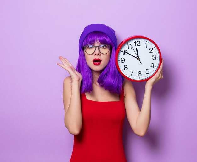 Porträt eines jungen Hipster-Mädchens mit lila Haaren und großer Uhr auf lila Hintergrund