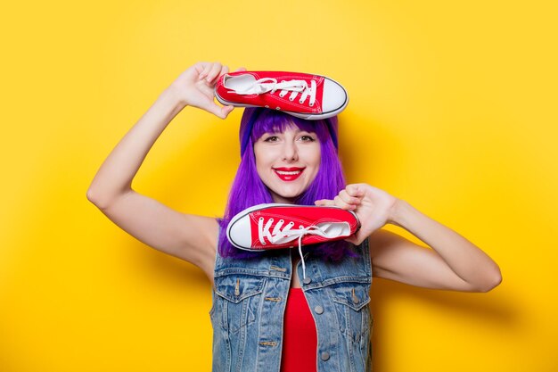 Porträt eines jungen Hipster-Mädchens mit lila Haaren und roten Gummischuhen auf gelbem Hintergrund