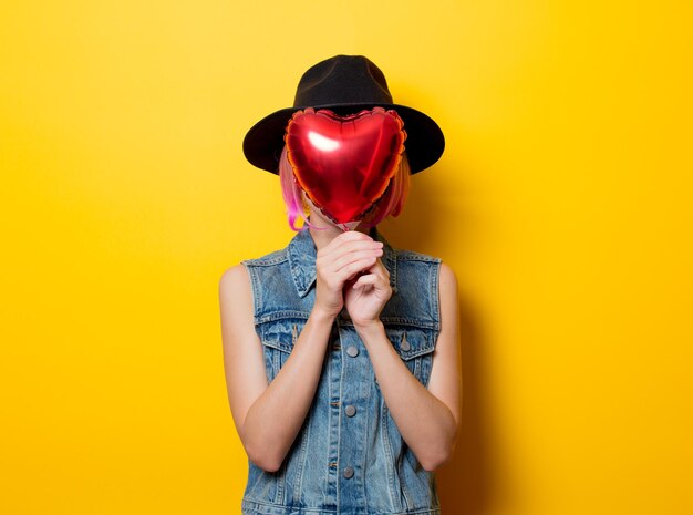 Porträt eines jungen Hipster-Mädchens mit rosa Frisur mit herzförmigem Ballon auf gelbem Hintergrund. Valentinstag