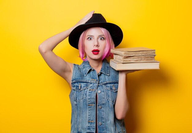 Porträt eines jungen Hipster-Mädchens mit rosafarbener Frisur mit Büchern auf gelbem Hintergrund