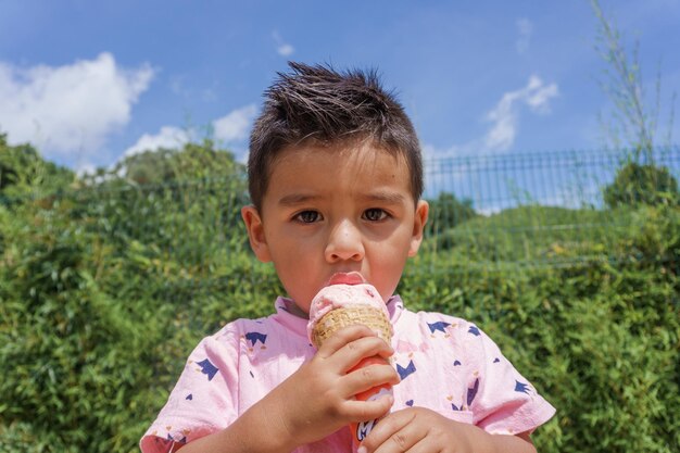 Porträt eines jungen hispanischen Kindes, das an einem sonnigen Tag eine Eistüte in einem Park isst