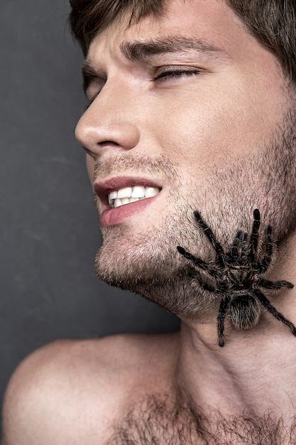 Porträt eines jungen hübschen Mannes mit Spinne auf seinem Gesicht