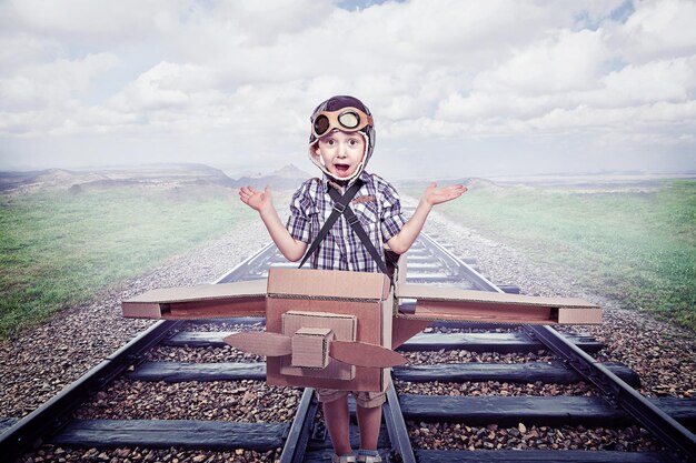 Foto porträt eines jungen in einem kartonflugzeug auf einer eisenbahnstrecke gegen den himmel