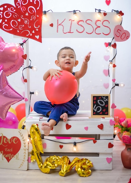 Porträt eines Jungen in einer Kusskabine, die mit Herzen und Luftballons geschmückt ist