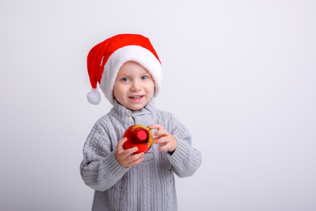 Porträt eines Jungen in Santa Claus-Hut, der einen Weihnachtsbaum-Spielzeugball hält