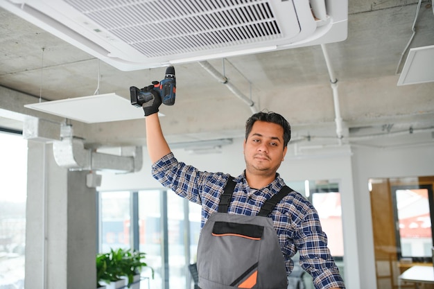 Porträt eines jungen indischen Technikers, der eine Klimaanlage repariert.
