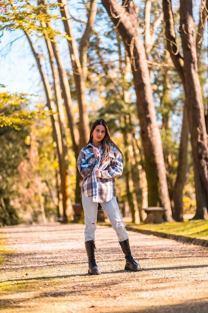 Porträt eines jungen kaukasischen brünetten Mädchens in einem karierten Wollpullover und zerrissenen Jeans in einem Park