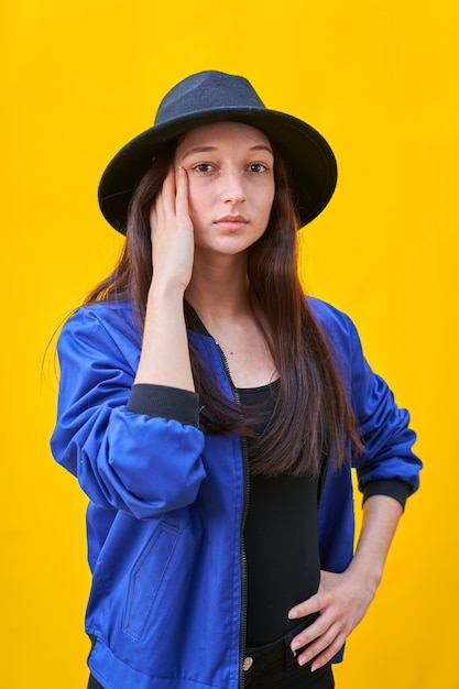 Porträt eines jungen kaukasischen Mädchens im schwarzen Hut und in der blauen Jacke, Hand über Gesicht