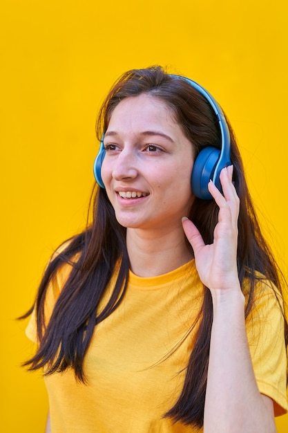 Porträt eines jungen kaukasischen mädchens mit langen braunen haaren, gelbem t-shirt, musik mit ihren blauen kopfhörern hörend.