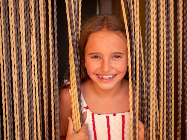 Porträt eines jungen kaukasischen Mädchens mit Zahnspange, das durch die Vorhänge lächelt