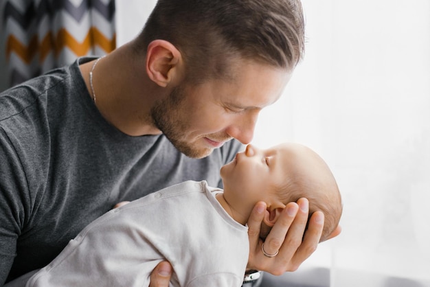 Porträt eines jungen kaukasischen Vaters, der seinen neugeborenen Sohn zu Hause hält