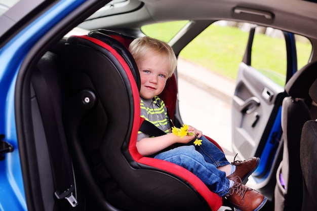 Porträt eines jungen Kindes eines Jungen mit blonden Haaren in einem Kinderautositz.
