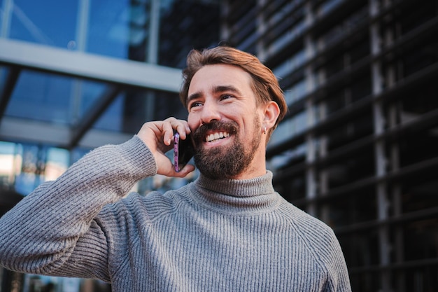 Porträt eines jungen, lächelnden, fröhlichen Unternehmers, der telefoniert und sich mit jemandem unterhält