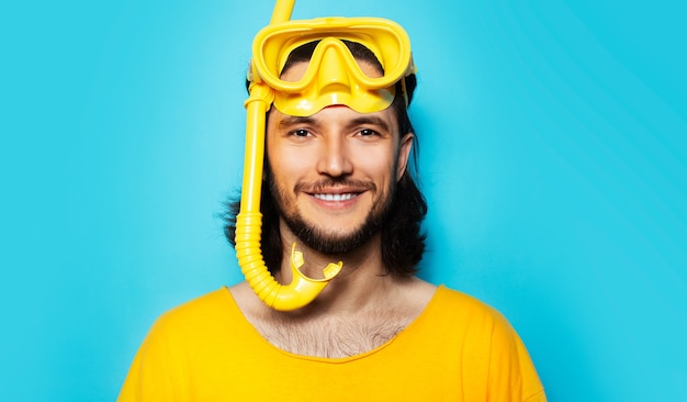 Porträt eines jungen lächelnden Mannes in gelb mit Taucherbrille und Schnorchel auf blauem Hintergrund.