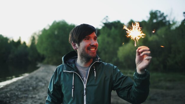 Porträt eines jungen lächelnden Mannes mit Wunderkerze, der auf einer Strandparty feiert