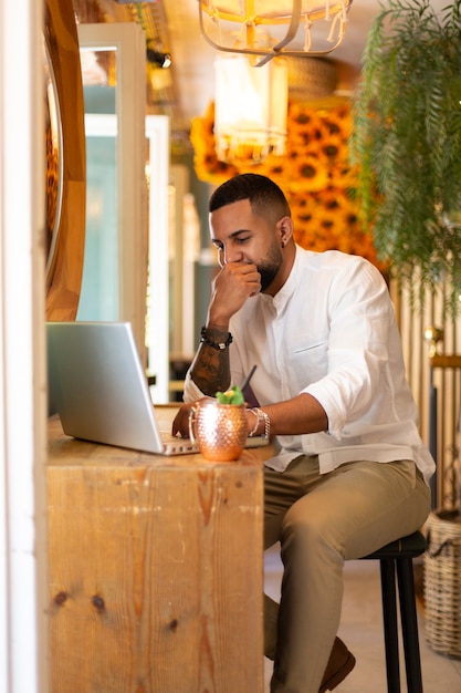 Porträt eines jungen lateinamerikanischen Mannes, der einen Laptop in einem modernen Café verwendet.