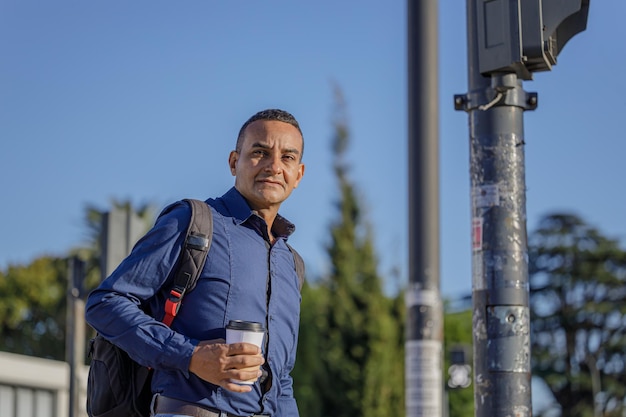 Porträt eines jungen Latino-Mannes mit einer Papptasse Kaffee in der Hand, der darauf wartet, die Straße zu überqueren