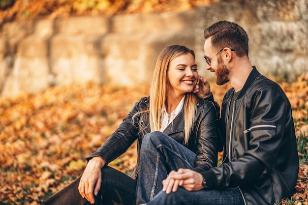 Porträt eines jungen liebenden Paares, das im Herbstblatt sitzt und Natur genießt