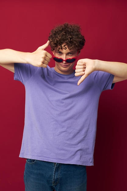 Porträt eines jungen, lockigen Mannes in einem lila T-Shirt mit Sonnenbrille, der isolierten Hintergrund posiert