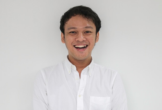 Porträt eines jungen, lustigen asiatischen Mannes mit weißem Hemd, der in die Kamera blickt und glücklich lächelt