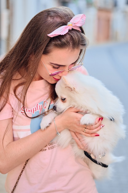 Porträt eines jungen Mädchens, das ihren weißen flaumigen pomeranian Hund küsst.