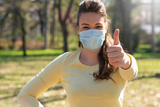 Foto porträt eines jungen mädchens mit maske, um sie vor dem corona-virus zu schützen, das den schlag hochhält