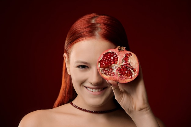 Porträt eines jungen Mädchens mit roten Haaren und Granatapfelfrüchten, die ihr Gesicht bedecken