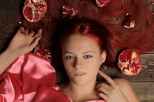 Foto porträt eines jungen mädchens mit roten haaren und granatapfelfrüchten im haar auf braunem hintergrund