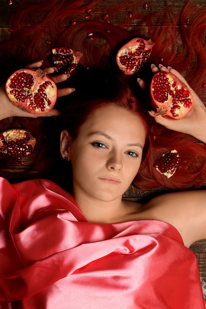 Porträt eines jungen Mädchens mit roten Haaren und Granatapfelfrüchten im Haar auf braunem Hintergrund