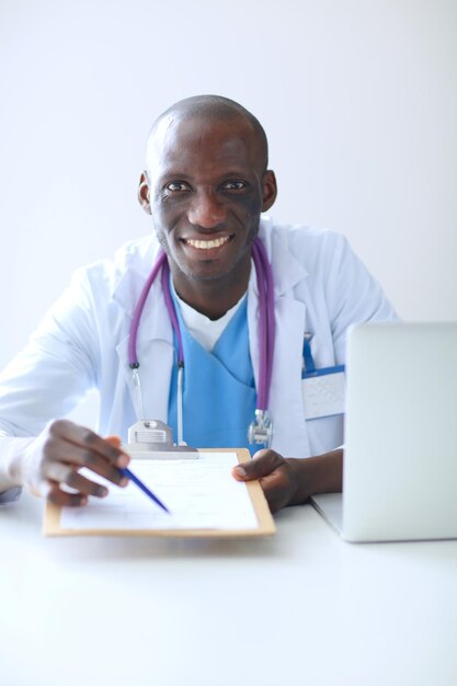 Porträt eines jungen männlichen Arztes, der ein Headset trägt, während er den Computer am Schreibtisch in der Klinik benutzt Doktor