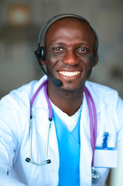 Porträt eines jungen männlichen Arztes mit Headset, während er den Computer am Schreibtisch in der Klinik benutzt