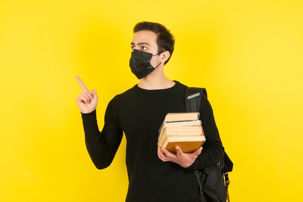 Porträt eines jungen männlichen Studenten in medizinischer Maske, der College-Bücher hält und zeigt