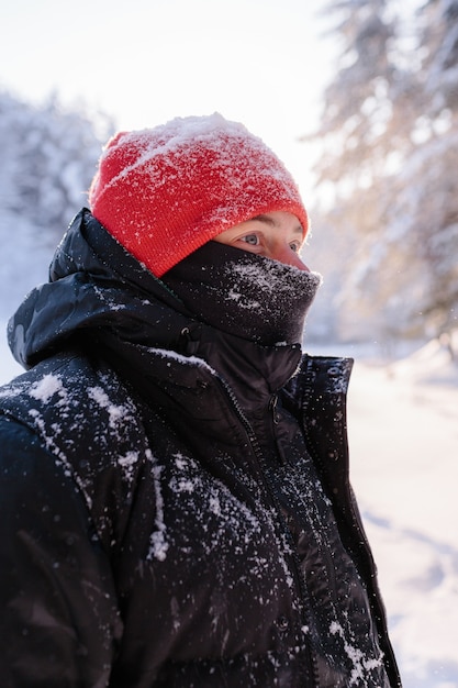 Porträt eines jungen Mannes an einem sonnigen Wintertag vor dem Hintergrund eines schneebedeckten Waldes