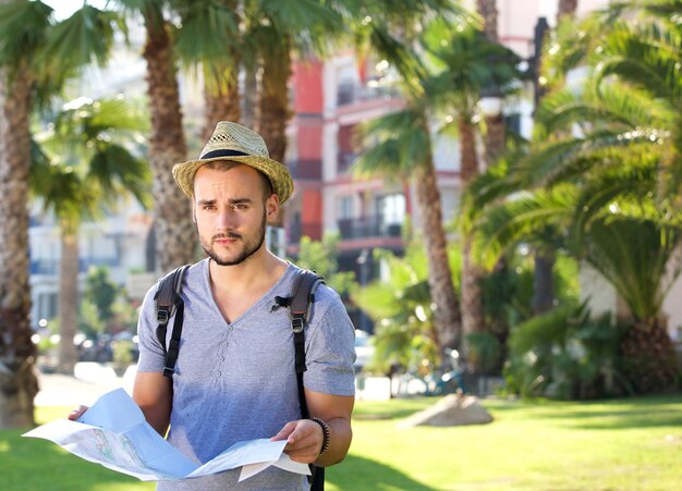 Porträt eines jungen Mannes, der alleine draußen mit Rucksack und Karte steht