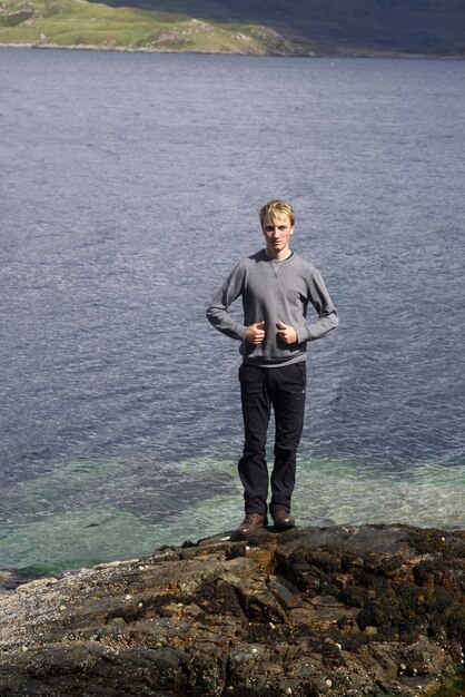 Foto porträt eines jungen mannes, der am meer auf einem felsen steht